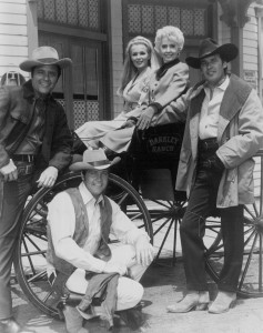 Cast photo from the television Western The Big Valley. From left: Richard Long, Linda Evans, Barbara Stanwyck, Peter Breck, and Lee Majors by wagon wheel.